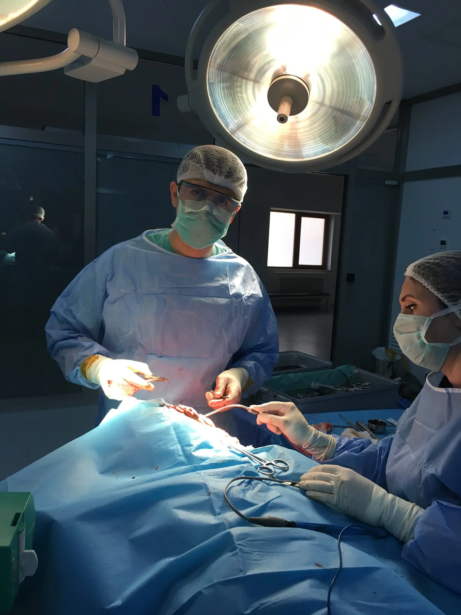 Böyüdücü eynək və baş işığı taxmış cərrah əməliyyatda, yanında tibb bacısı