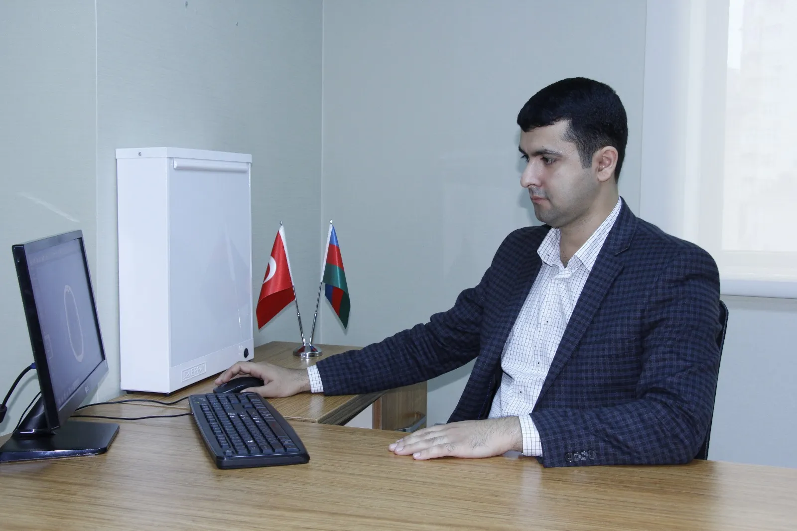 Dr. Ruslan Yunusov kabinetdə kompüter qarşısında, masada Azərbaycan və Türkiyə bayraqları